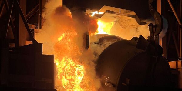 Aus der Stahlpfanne wird der flüssige Stahl ausgeschüttet. Dabei entstehen große Flammen und Rauch.