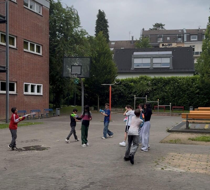 Mit Wasserpistolen und Wasserbomben machen sich acht Schülerinnen und Schüler gegenseitig nass.