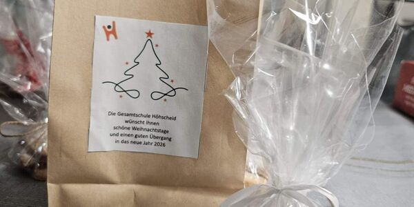 Auf einem Tisch steht eine Papiertüte mit Weihnachtsaufkleber und davor Plätzchen in Folie eingepackt.