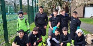 10 Jungs machen ein Mannschaftsfoto neben dem Sportplatz. Alle haben schwarze Trikots und Hasen mit neongrünen Stutzen an.