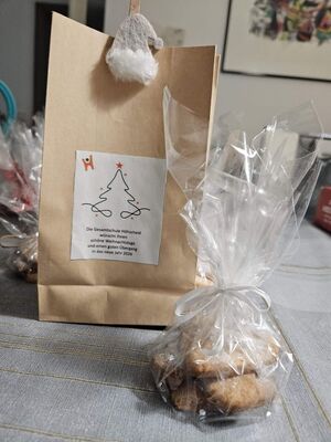 Auf einem Tisch steht eine Papiertüte mit Weihnachtsaufkleber und davor Plätzchen in Folie eingepackt.