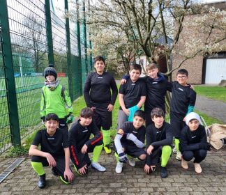 10 Jungs machen ein Mannschaftsfoto neben dem Sportplatz. Alle haben schwarze Trikots und Hasen mit neongrünen Stutzen an.